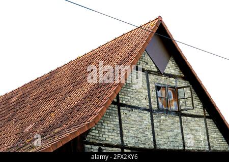 Old half-timbered barn. Weathered building with an old open window. Roof with red roof tiles Stock Photo