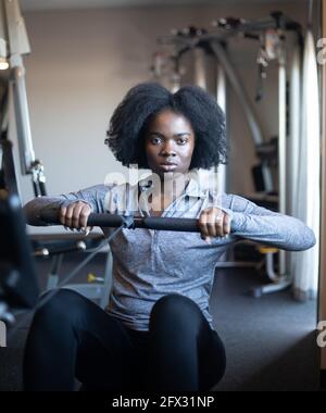Woman doing cardio workout on rowing machine in gym. female exercising, one person, African American, natural hair, black woman, gym fitness, color Stock Photo