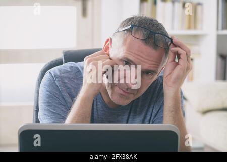 Tired and overworked freelancer holding his head in hand while sitting at his working place in the office or home Stock Photo