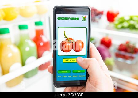Man using smart phone, buying food. Close-up hand with phone. Grocery shopping online. Mobile app of online food store. Fresh vegetables in fridge Stock Photo