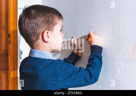 The child draws on the wall with colored chalk. The boy is engaged in creativity at home Stock Photo