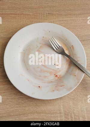 Dirty empty plate and fork after dinner on wooden table Stock Photo