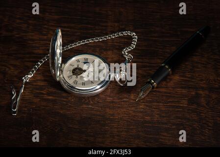 Watch vintage pocket  and fountain pen in close-up on rustic wooden surface. Stock Photo