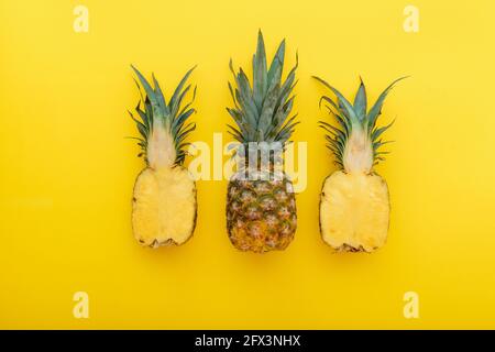 Pineapple fruit on yellow summer background. A whole tropical pineapple and half fruit in a minimalist style on a summer bright yellow background Stock Photo