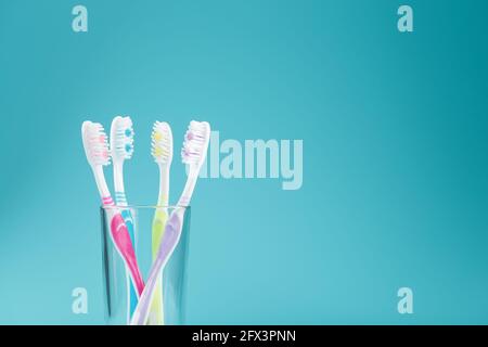 Toothbrushes of different colors in a transparent glass on a blue background. The concept of oral health care for the whole family. Free space Stock Photo