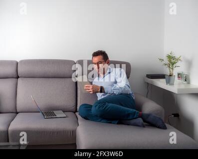 Caen, France, May 2021. The man works remotely on the iPad and sits on the computer on the sofa, the new normality is working from home. Stock Photo