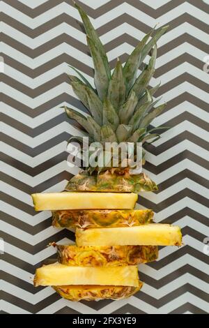 Sliced pineapple on graphic summer background. Tropical fruit sliced pineapple rings. Creative flat lay composition on black and white stripes pattern Stock Photo