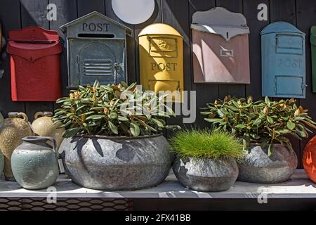 Selection of clay amphorae and pots of various shapes and colors on a shelf against the background of decorative mailboxes hanging on a shabby wall Stock Photo