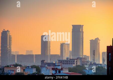 dawn shot of skyscrapers houses shot partially hidden in fog with the warm orange of dusk showing the start of a new day in gurgaon, delhi, india Stock Photo