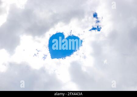 In the snow-white clouds in the gap there is a heart from the blue sky, an angel is nearby. Place for your text. Concept of love, god, fulfillment of desires. Stock Photo