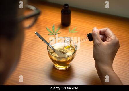 Woman pouring CBD oil in a natural infusion. Using CBD, natural remedy made with cannabis. Stock Photo