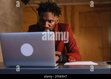 a focused black man in a suit is working on a laptop. Remote work from home Stock Photo