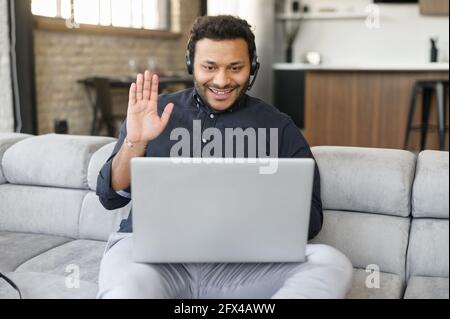 Indian businessman wearing headset using laptop computer for connection with colleagues, customers, hispanic mixed-race man waving into webcam, working remotely, staying at home Stock Photo