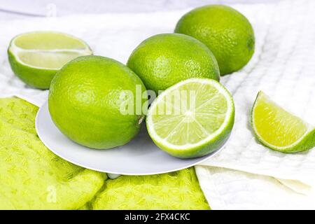 Fresh green juicy limes and lime slices in the kitchen on light background. Stock Photo