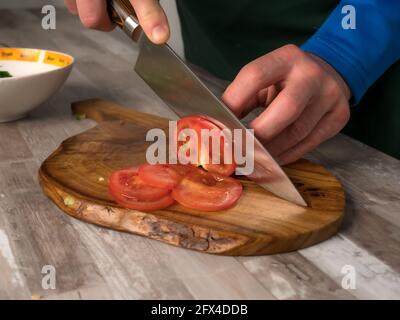 Cutting a tomato with a knife on a wooden board, close-up photo, warm color of the photo Stock Photo