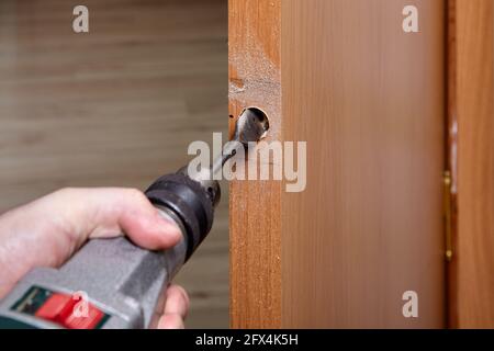 Locksmith drills hole for door lock with knob. Stock Photo
