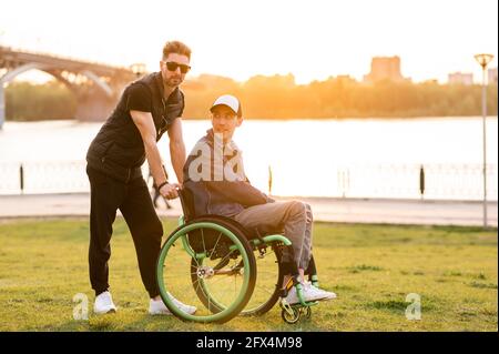 Help for people with physical disabilities. Man drive wheelchair and help his friend. Social services for population. Stock Photo