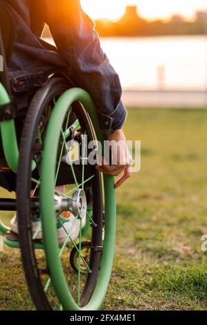 A disabled man is sitting in a wheelchair. He holds his hands on the wheel. Stock Photo