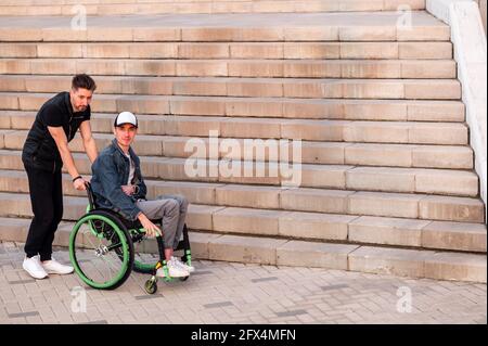 Help for people with physical disabilities. Man drive wheelchair and help his friend. Social services for population. Stock Photo