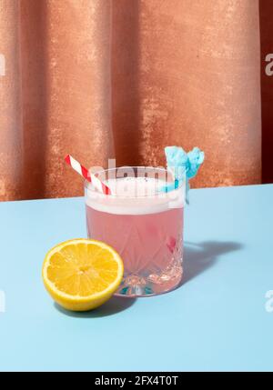 Fun cocktail drink for a party on colored background. Velvet and pale blue. Lemon and straw with flare. Stock Photo