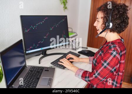 Woman working from home as a trader, types on the keyboard while looking at a monitor with graphics Stock Photo