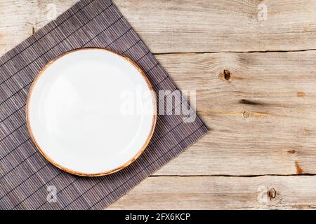 Empty white ceramic dish on rustic wooden table with brown bamboo mat Stock Photo