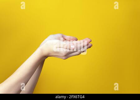 Close-up of well-groomed delicate female hands with folded palms in boat raised up on yellow background. Gesture to collect water in palm of hand or t Stock Photo