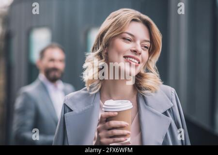 Happy young woman with coffee and man at distance Stock Photo