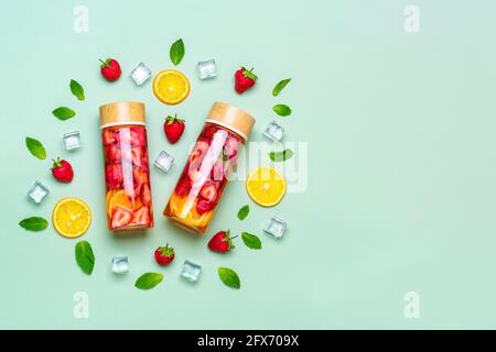 Strawberry infused water, cocktail, lemonade or tea. Summer iced cold drink with strawberry, lemon and lef of mint on green background. Flat lay Stock Photo