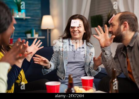 Mixed race friends socializing during entertainment party while playing guess who game attaching stickey notes. Multiracial people spending time together having fun during entertainment wekeend. Stock Photo