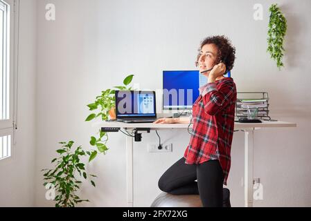 Woman teleworking at an adjustable standing desk with one knee resting on a fitball Stock Photo