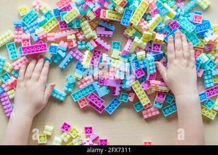 Hands of little kid playing with toy plastic building blocks on the table. Small child plays fun creative leisure activity at home or kindergarten. De Stock Photo