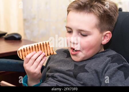 A Hungry boy eating a hot dog at home kid eats a hot-dog sandwich.Indoors shot.Closeup. Stock Photo