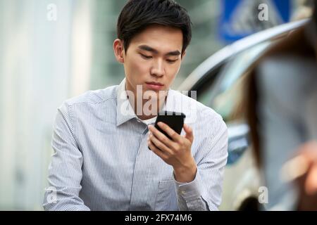 young asian office worker reading using cellphone outdoors Stock Photo