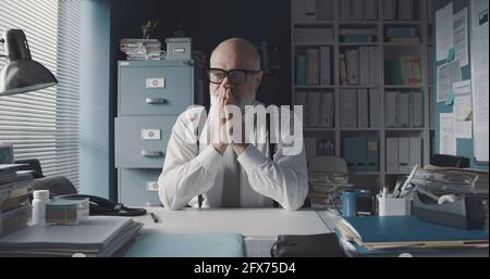 Worried stressed businessman sitting at office desk and thinking Stock Photo