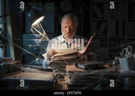 Corporate businessman searching for paperwork in an abandoned office: failure, financial crisis and outdated business concept Stock Photo