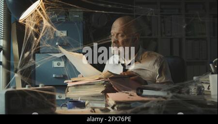 Corporate businessman searching for paperwork in an abandoned office: failure, financial crisis and outdated business concept Stock Photo