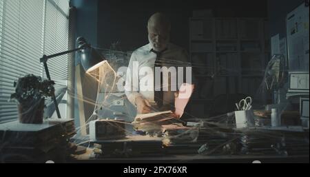 Corporate businessman searching for paperwork in an abandoned office: failure, financial crisis and outdated business concept Stock Photo