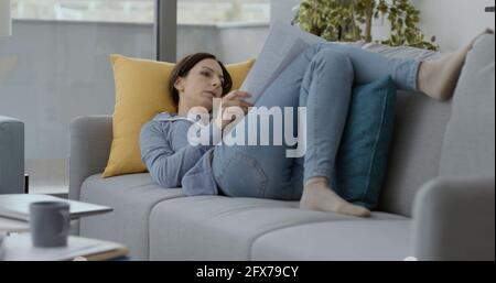 Woman lying on the sofa at home and checking paperwork, remote work concept Stock Photo