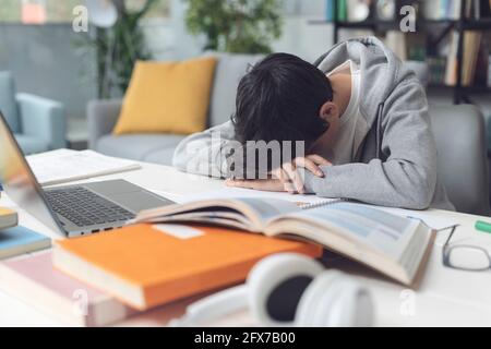 Tired student falling asleep over the desk, he is sad and exhausted Stock Photo