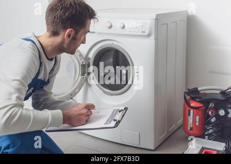 Professional technician checking a washing machine, he is writing on a clipboard Stock Photo