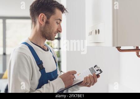 Professional plumber checking a boiler at home and writing on a clipboard Stock Photo