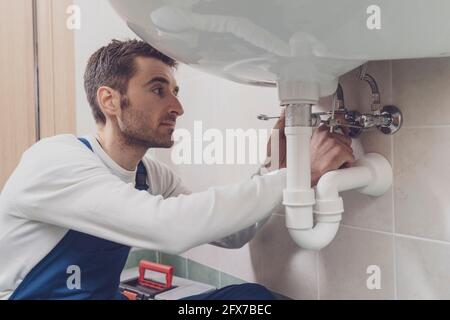 Professional plumber fixing a sink at home, he is checking pipes with a wrench Stock Photo