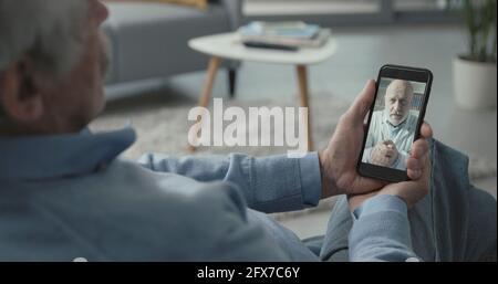 Senior man video calling his online doctor from home, telemedicine concept Stock Photo