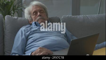 Senior man sitting on the couch at home and sleeping Stock Photo