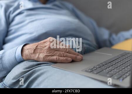 Senior man sitting on the sofa and using a laptop, hand close up Stock Photo