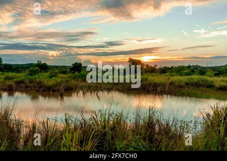 Scenic view of beautiful sunset above the lake at summer cloudy sky and grass field. Landscape of sunset and blue sky reflected on water Stock Photo