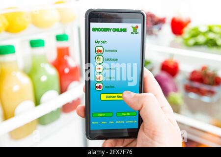 Man using smart phone, buying food. Close-up hand with phone. Grocery shopping online. Mobile app of online food store. Fresh vegetables in fridge Stock Photo