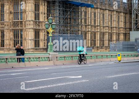London. UK- 05.23.2021. A rider for the online food order company Deliveroo cycling  on Westminster Bridge by Westminster Palace on the way to make a Stock Photo