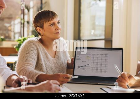 Female business professional giving presentation to colleagues on laptop. businesswoman listening to team members in meeting. Stock Photo
